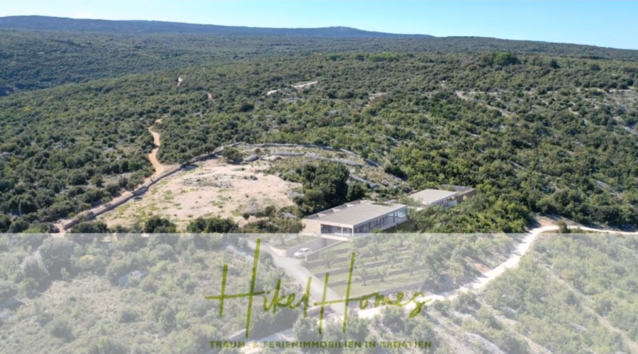 2 Meerblick Rohbau-Villen mit Haupt- und Gästehaus in absoluter privater Lage - Luftaufnahme eines großen, modernen Hauses in einer üppigen, grünen Hügellandschaft. Ein Feldweg schlängelt sich durch die Vegetation. Der Himmel ist klar, und der Horizont erstreckt sich über das Bild. Unten im Bild sind die Texte „Hikel Homes“ und „Traumhafte Feriendomizile in Kroatien“ eingeblendet. (42502)