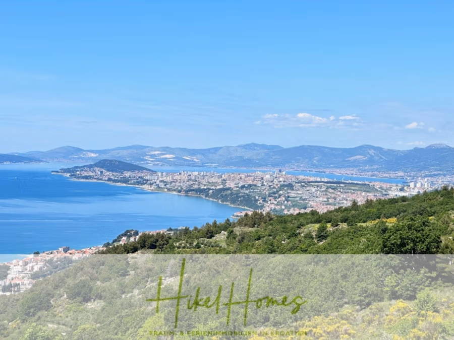 Exklusive 380m² Meerblick & Luxus in absoluter Alleinlage mit Privatspähre + Pool, Sommerküche, … - Eine malerische Küstenansicht mit einer Stadt am Meer, Hügeln im Vordergrund und Bergen in der Ferne unter einem klaren blauen Himmel. Das Bild enthält den Text „Hike Homes“. (41903)