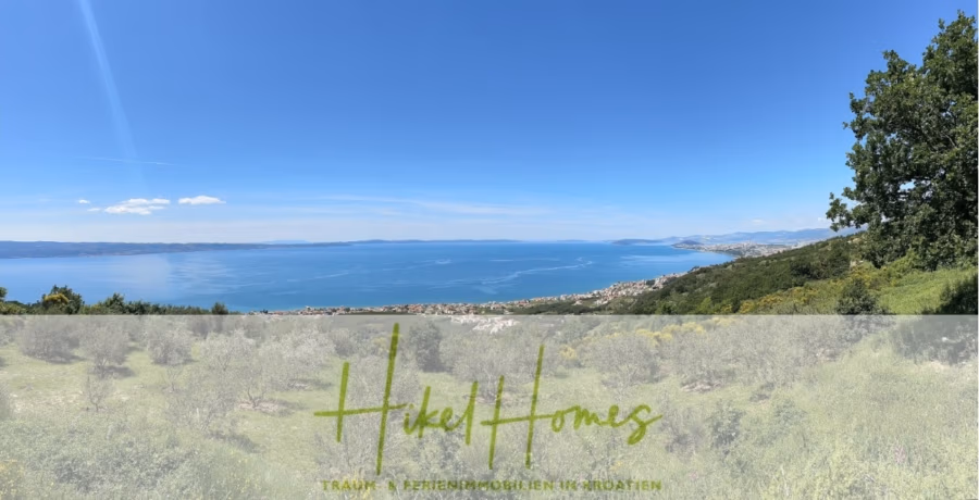 Exklusive 380m² Meerblick & Luxus in absoluter Alleinlage mit Privatspähre + Pool, Sommerküche, … - Ein Panoramablick auf eine Küstenlandschaft mit Meer unter klarem, blauem Himmel. Grünflächen und wilde Vegetation stehen im Vordergrund, in der Ferne erstrecken sich Berge und eine Küstenlinie am Horizont. Unten ist der Text „Hikel Homes“ eingeblendet. (41902)