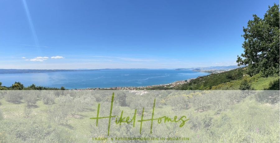 Exklusive 380m² Meerblick & Luxus in absoluter Alleinlage mit Privatspähre + Pool, Sommerküche, … - Panoramablick auf ein blaues Meer mit fernen Bergen und einer Küstenstadt, gesehen von einem grünen Hügel aus unter einem klaren blauen Himmel. Der Schriftzug "Hikel Homes" und ein deutscher Text sind am unteren Rand eingeblendet. (44522)