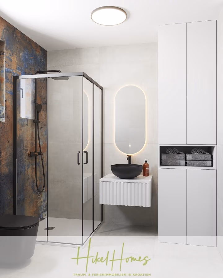 Meerblick 76m² Neubauwohnung mit 2 Schlafzimmer, Balkon und Südausrichtung - Modernes Badezimmer mit verglaster Duschkabine, schwarzen Armaturen und einem schwarzen Waschbecken auf einem weißen Waschtisch. Ein hoher Schrank enthält gefaltete graue Handtücher. Die Wände bestehen aus glattem Beton und einer strukturierten Platte. Eine runde Deckenleuchte erhellt den Raum. (41371)