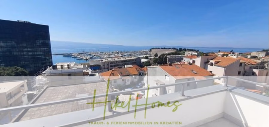 Charmantes 1-Zimmer-Appartement mit Meerblick im Herzen von Split mit Dachterrasse - Blick von einem Balkon auf eine Küstenstadt in Kroatien. Weiße Gebäude mit roten Dächern, ein Yachthafen voller Boote und das Meer unter einem klaren blauen Himmel sind zu sehen. Im Vordergrund ist ein Glasgeländer zu sehen, darunter ein Teil des Logos. (42234)