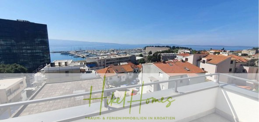 Charmantes 1-Zimmer-Appartement mit Meerblick im Herzen von Split mit Dachterrasse - Blick von einem Balkon auf die Dächer, einen Jachthafen mit Booten und das Meer. Ein modernes Gebäude befindet sich auf der linken Seite, mit klarem Himmel und Bergen im Hintergrund. Der Text am unteren Rand lautet "Hikel Homes - Traum- & Ferienimmobilien in Kroatien. (45421)