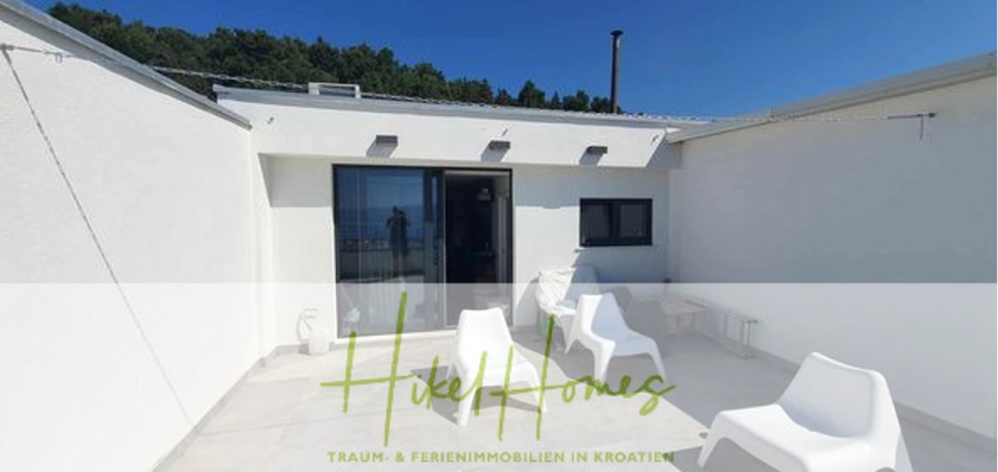 Charmantes 1-Zimmer-Appartement mit Meerblick im Herzen von Split mit Dachterrasse - Sonnige Dachterrasse mit weißen Wänden, einer Glastür und modernen weißen Stühlen. Das Spiegelbild einer Person ist in der Tür sichtbar. "Hotel Homes" und deutscher Text über Traum- und Ferienimmobilien in Kroatien überlagern das Bild. (45417)