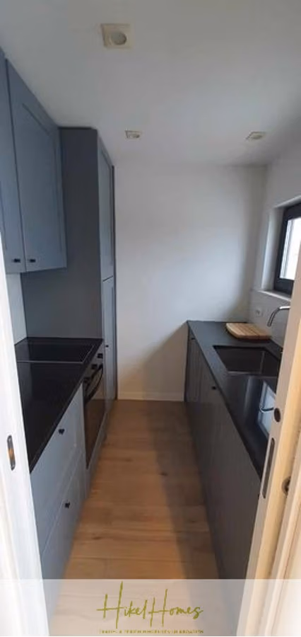 Charmantes 1-Zimmer-Appartement mit Meerblick im Herzen von Split mit Dachterrasse - Eine schmale, moderne Küche mit dunkelgrauen Schränken, schwarzen Arbeitsplatten und hellem Holzboden. Sie verfügt über einen Einbaubackofen und eine Spüle unter einem Fenster. Der Raum ist kompakt und dennoch funktional. (42224)