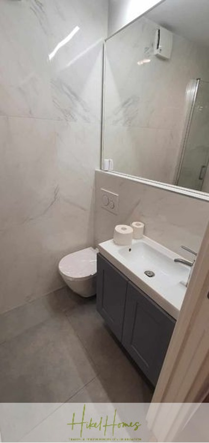 Charmantes 1-Zimmer-Appartement mit Meerblick im Herzen von Split mit Dachterrasse - Ein modernes Badezimmer mit einer an der Wand befestigten Toilette, einem grauen Waschtisch mit weißem Waschbecken, zwei Rollen Toilettenpapier, einem großen Spiegel und hell gefliesten Wänden und Böden. (45414)
