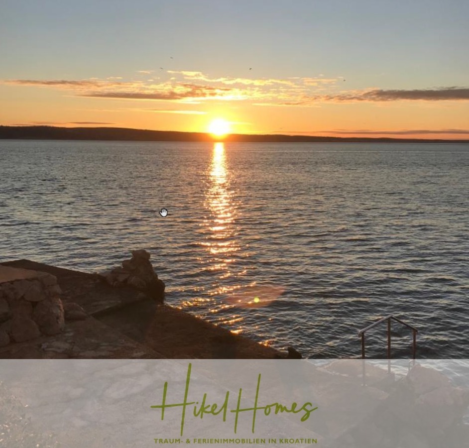 Sonnenuntergang über einem ruhigen Meer mit sanften Wellen, einer felsigen Uferlinie auf der linken Seite und Metallstufen, die ins Wasser führen. Der Himmel ist teilweise bewölkt, und am unteren Rand steht "Hikel Homes". - 1160m² in erste Reihe zum Meer / Ideal zur Bebauung mit 2 Villen in erster und zweiter Reihe