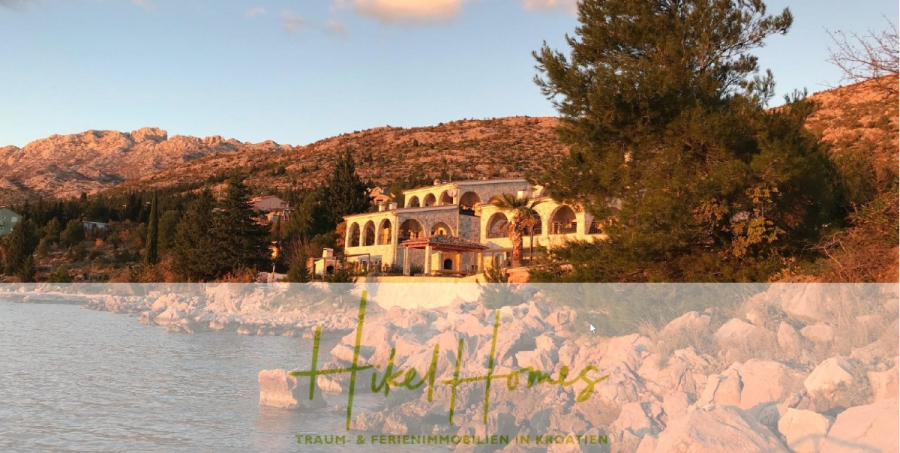 1160m² in erste Reihe zum Meer / Ideal zur Bebauung mit 2 Villen in erster und zweiter Reihe - Eine große Villa mit Bögen und Balkonen liegt zwischen Bäumen und felsigen Hügeln mit Blick auf ein ruhiges Gewässer bei Sonnenuntergang. Der Text "Hikel Homes: Traum- & Ferienimmobilien in Kroatien" überlagert das Bild. (46000)