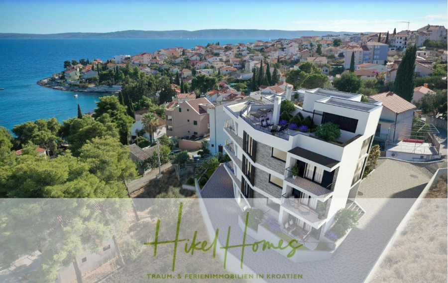 Luxus Meerblick 77m² Ensemble mit 2 Schlafzimmern, Terrasse und Südausrichtung – Einziehen 2025! - Ein modernes, weißes Apartmentgebäude mit Blick auf die Adria in einer kroatischen Küstenstadt, umgeben von Häusern, Grün und klarem, blauem Wasser unter einem sonnigen Himmel. Auf dem Bild ist der Text zu lesen: "Hikel Homes Traum- & Ferienimmobilien in Kroatien. (46453)