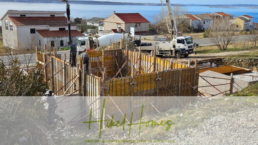 Neubau Meerblick 270m vom Meer entfernt – Hochwertigen Ausstattung – Fertigstellung Ende 2025 - Bauarbeiter errichten ein Hausfundament mit Holz- und Metallgerüsten in der Nähe einer Straße am Meer; ein Zementlaster und ein Kran sind zu sehen, im Hintergrund Häuser und das Meer. (46243)