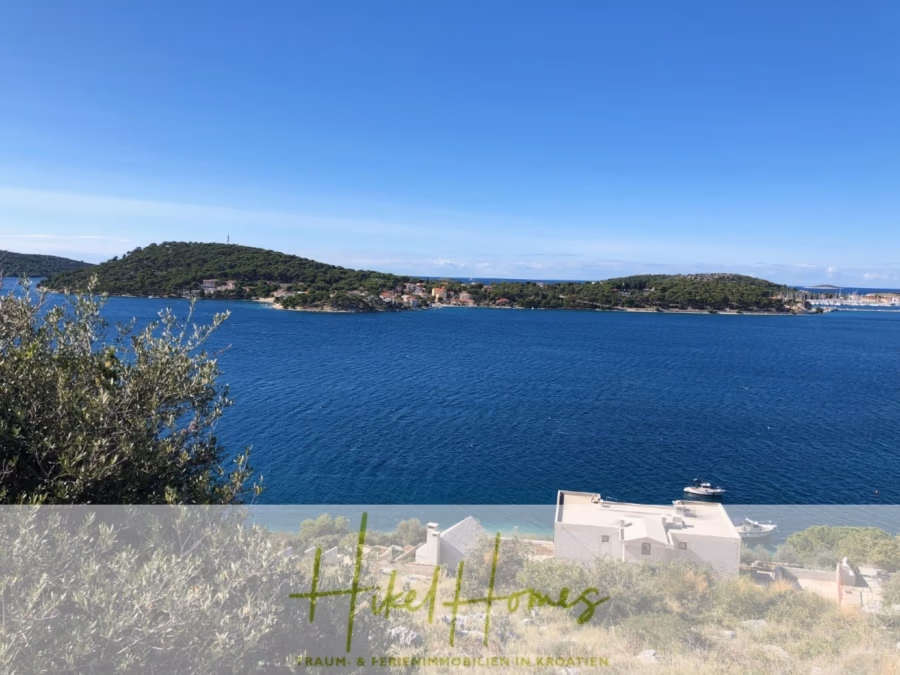 Luxus Villa Sunce / gegenüber Marina Frapa / Meerblick + direkter Meerzugang, Pool, mit 391m² WFL - Ein malerischer Blick auf eine Küstenregion mit blauem Wasser und grünen Hügeln. Entlang der Küste sind Häuser zu sehen. Der Himmel ist klar und sonnig. Bäume im Vordergrund rahmen die Landschaft ein. (42033)