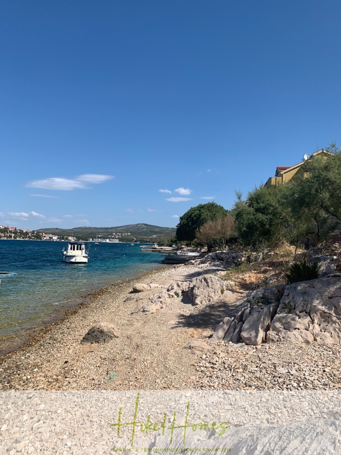 Luxus Villa Sunce / gegenüber Marina Frapa / Meerblick + direkter Meerzugang, Pool, mit 391m² WFL - Felsige Küste mit klarem blauen Wasser, ein weißes Boot, das in der Nähe der Küste schwimmt, verstreute Bäume und Häuser auf der rechten Seite unter einem strahlend blauen Himmel. Der Text "Hotel Homes" erscheint am unteren Rand des Bildes. (45126)