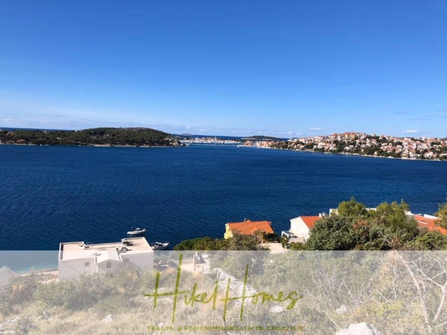 Luxus Villa Sunce / gegenüber Marina Frapa / Meerblick + direkter Meerzugang, Pool, mit 391m² WFL - Malerischer Küstenblick auf eine große, ruhige blaue Bucht mit kleinen Booten und Küstenhäusern. Im Vordergrund sind Sträucher und Dächer zu sehen, während im Hintergrund ein baumbedeckter Hügel und eine entfernte Stadt unter einem klaren blauen Himmel zu sehen sind. (42034)