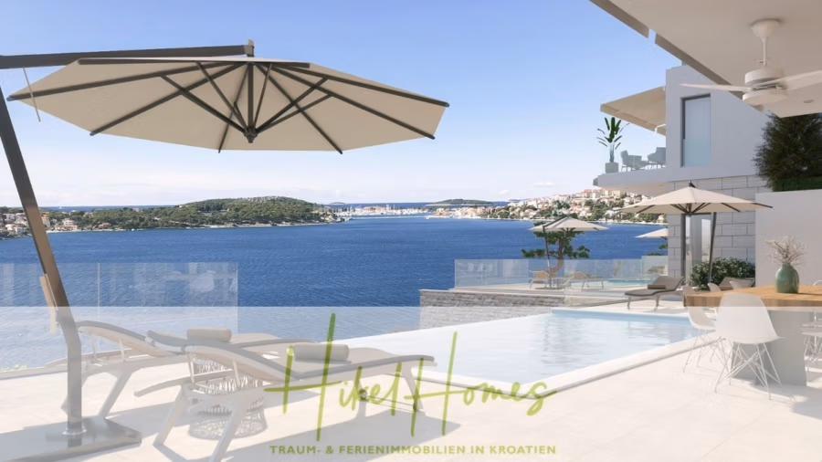 Luxus Villa Sunce / gegenüber Marina Frapa / Meerblick + direkter Meerzugang, Pool, mit 391m² WFL - Eine luxuriöse Terrasse mit herrlichem Blick auf die Küste bietet Sonnenliegen, Sonnenschirme und einen Infinity-Pool. Am Horizont ist eine Stadt mit Gebäuden und üppigen Bäumen zu sehen. (42019)