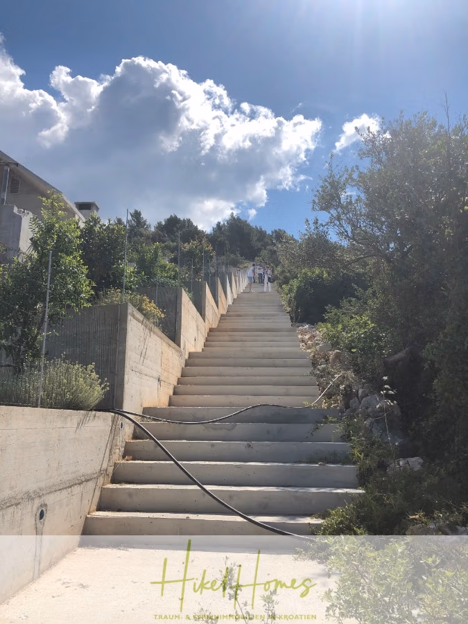 Luxus Villa Sunce / gegenüber Marina Frapa / Meerblick + direkter Meerzugang, Pool, mit 391m² WFL - Eine steile Betontreppe im Freien mit Handlauf führt hinauf in den hellen, sonnigen Himmel. Auf beiden Seiten ist sie von Grün und Sträuchern umgeben, oben sind einige Menschen zu sehen. Über die unteren Stufen ist ein Schlauch gelegt. (42023)