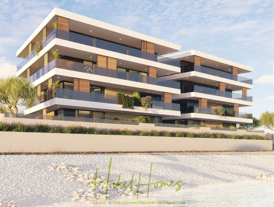 1. Reihe hochwertige Neubau-Meerblick Wohnung mit 2 SZ, Terrasse und Gemeinschaftspool (S1B) - Modernes, dreistöckiges Apartmentgebäude am Strand mit großen Glasbalkonen, umgeben von Grün und Palmen, vor blauem Himmel, mit "Holiday Homes" und deutschem Text am unteren Rand. (46146)