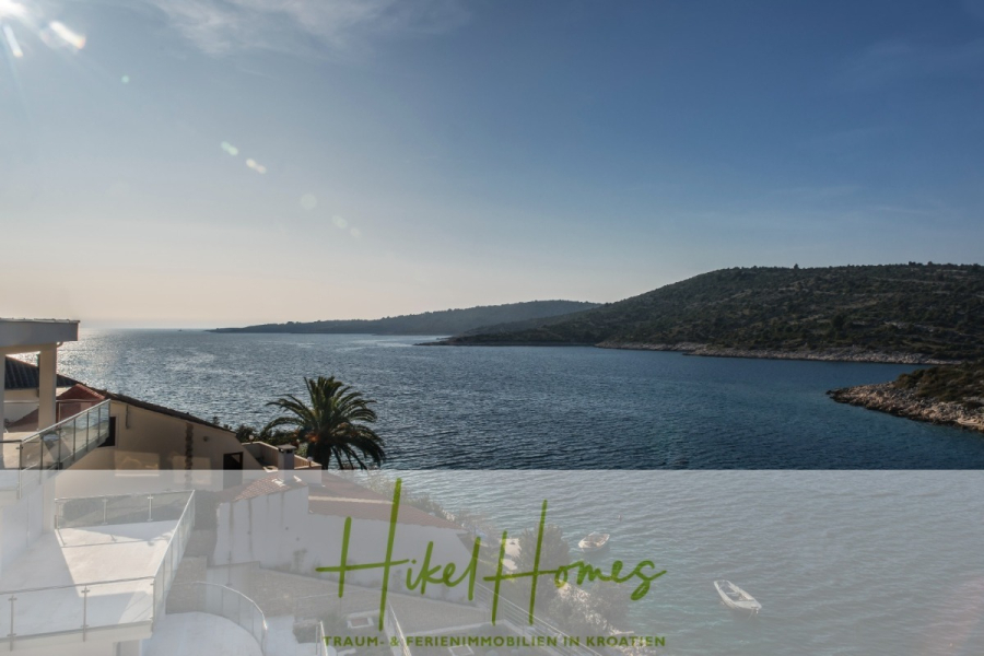 5 Sterne Luxus Villa Christina – 250m² WFL in 1. Reihe zum Meer/ 4 SZ / Neubau / Sofort bezugsfertig - Blick auf eine ruhige Bucht mit klarem, blauem Wasser, grünen Hügeln, Booten und einer Palme, gesehen von einem Balkon. Der Text "Hikel Homes" und "TRAUM-FERIENIMMOBILIEN IN KROATIEN" ist am unteren Rand eingeblendet. (46305)