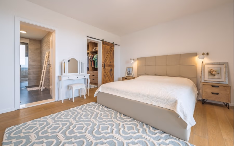 Villa am Stadtrand von Split großzügige Aufteilung, hohe Räume und beheiztem Pool - Ein gemütliches Schlafzimmer mit einem großen Bett mit gepolstertem Kopfteil und weißer Bettwäsche. Ein gemusterter Teppich bedeckt den Holzboden. Das Zimmer verfügt über einen Schminktisch mit Spiegel, eine hölzerne Schiebetür und zwei kleine Beistelltische. Eine Tür führt zum Badezimmer. (41930)