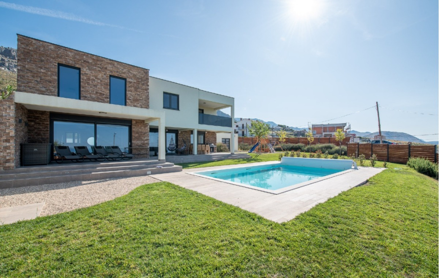 Villa am Stadtrand von Split großzügige Aufteilung, hohe Räume und beheiztem Pool - Modernes zweistöckiges Haus mit weißem Backstein, großen Fenstern und einem Garten mit rechteckigem Swimmingpool, grünem Rasen, Terrassenstühlen und einem sonnigen, klaren Himmel. (46555)