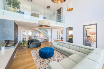 Geräumiges, modernes Wohnzimmer mit hellen Wänden, großen Fenstern, einem Sektionssofa, einer blauen Ottomane, einem gemusterten Teppich und einem offenen Zwischengeschoss. Glastreppengeländer, Holzböden und stilvolle Beleuchtung vervollständigen das luftige Interieur. - Villa am Stadtrand von Split großzügige Aufteilung, hohe Räume und beheiztem Pool