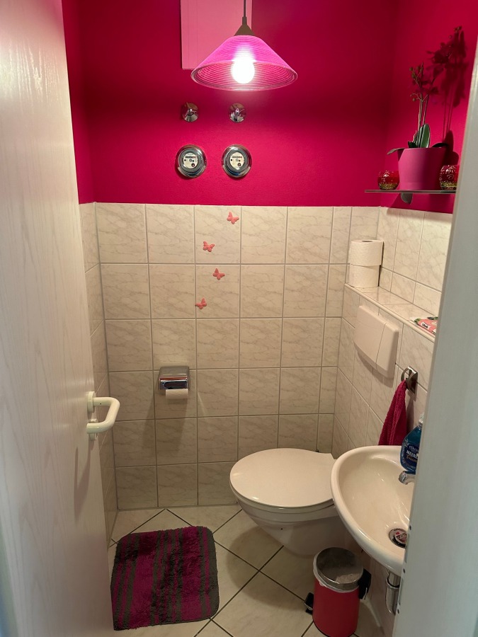 Provisionsfrei: 3,5 Zimmer Wohnung 90m² / 150m vom Bodensee entfernt mit Garten, Garage, … - Ein kleines Badezimmer mit weißen Fliesen und leuchtend rosafarbenen Wänden, einer weißen Toilette und einem Waschbecken, einer rosafarbenen Leuchte, rosafarbenem Dekor, einem rosafarbenen Teppich, einem rosafarbenen Mülleimer und rosafarbenen Schmetterlings-Wandaufklebern. (45573)