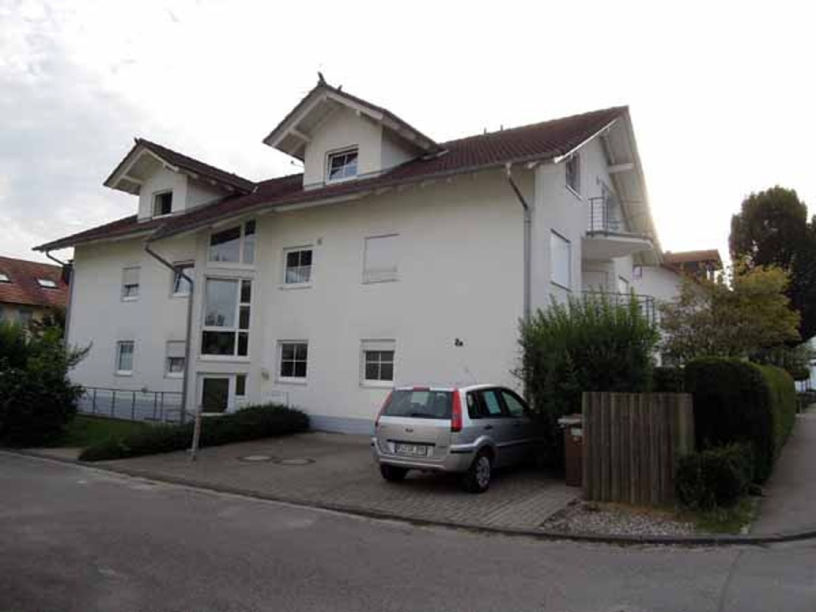 Provisionsfrei: 3,5 Zimmer Wohnung 90m² / 150m vom Bodensee entfernt mit Garten, Garage, … - Ein kleines silbernes Auto parkt vor einem modernen, weißen, zweistöckigen Wohnhaus mit rotem Ziegeldach, umgeben von Grünflächen und einer ruhigen Straße. (45566)