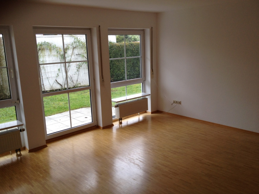 Provisionsfrei: 3,5 Zimmer Wohnung 90m² / 150m vom Bodensee entfernt mit Garten, Garage, … - Leerer Raum mit hellem Holzboden, weißen Wänden und großen Fenstern, die auf einen grasbewachsenen Hinterhof blicken. Unter den Fenstern befinden sich Heizkörper, und das Sonnenlicht erhellt den Raum. Es sind keine Möbel vorhanden. (45569)