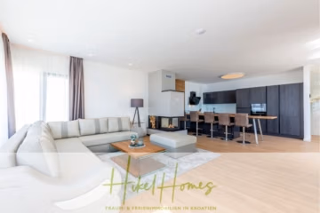 Ein geräumiges, modernes Wohnzimmer mit einem großen beigefarbenen Sofa und einem Couchtisch aus Holz. Der offene Raum umfasst eine Küche mit dunklen Schränken und einen Essbereich. Heller Holzboden und große Fenster sorgen für eine freundliche Atmosphäre. - Ein Paradies mit atemberaubendem Meerblick! 4 SZ, Pool, Solar, …