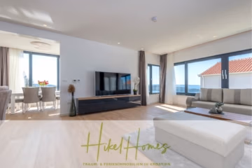 Modernes, lichtdurchflutetes Wohnzimmer mit hellem Holzboden und großem Flachbildfernseher. Der angrenzende Essbereich verfügt über einen Tisch und Stühle. Große Fenster bieten Meerblick. Der Raum ist mit schlichten, eleganten Möbeln und Pflanzen dekoriert. - Ein Paradies mit atemberaubendem Meerblick! 4 SZ, Pool, Solar, …