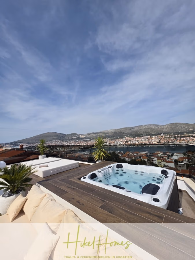 Luxus trifft Meerblick – Ein Anwesen der Extraklasse – Sofort einziehen - Eine Dachterrasse mit Whirlpool und Sonnenliegen bietet Aussicht auf eine Küstenstadt mit Bergen im Hintergrund und einem teilweise bewölkten Himmel. (43707)