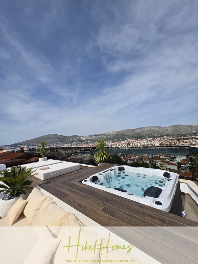 Luxus trifft Meerblick – Ein Anwesen der Extraklasse – Sofort einziehen - Eine Dachterrasse mit Whirlpool, Sitzgelegenheiten und Topfpflanzen bietet einen Blick auf eine Küstenstadt und Berge unter einem blauen Himmel mit Wolkenfetzen. Der Text am unteren Rand lautet: "Heike Homes Traum- & Ferienimmobilien in Kroatien. (46615)