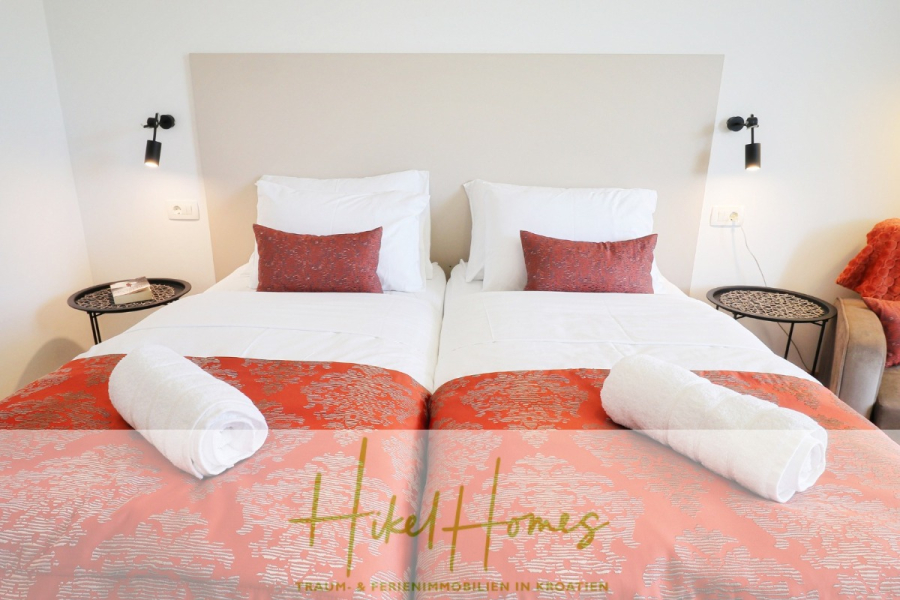 340m² Villa mit Pool auf der Insel Ciovo – vollständig möbiliert – auch Boutiquehotel möglich - Zwei sauber gemachte Einzelbetten mit weißer Bettwäsche, orange gemusterten Läufern und passenden Kissen. Auf jedem Bett liegen aufgerollte Handtücher. An der Wand befestigte Leselampen und kleine runde Nachttische flankieren die Betten. (45546)
