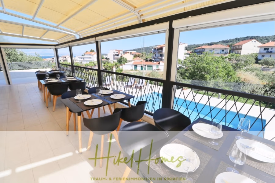 340m² Villa mit Pool auf der Insel Ciovo – vollständig möbiliert – auch Boutiquehotel möglich - Ein überdachter Essbereich im Freien bietet Tische mit weißen Tellern und Gläsern. Hinter dem Geländer bietet sich ein Blick auf den Pool und die benachbarten Häuser. Die Umgebung ist sonnig und von viel Grün umgeben. (41625)