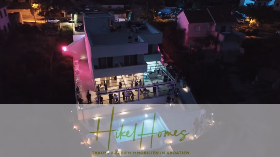 340m² Villa mit Pool auf der Insel Ciovo – vollständig möbiliert – auch Boutiquehotel möglich - Luftaufnahme eines modernen, mehrstöckigen Hauses bei Nacht, beleuchtet mit bunten Lichtern. Menschen haben sich auf dem Balkon und rund um den Poolbereich versammelt. Der Text lautet: „Hikel Homes“ mit einem deutschen Slogan darunter. (41640)