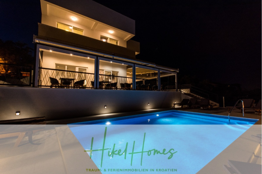 340m² Villa mit Pool auf der Insel Ciovo – vollständig möbiliert – auch Boutiquehotel möglich - Modernes zweistöckiges Haus bei Nacht mit einer großen Terrasse und Sitzgelegenheiten im Freien, beleuchtet von warmen Lichtern. Ein Swimmingpool im Vordergrund reflektiert die Beleuchtung. Der Schriftzug "Hikel Homes" erscheint am unteren Rand. (45550)