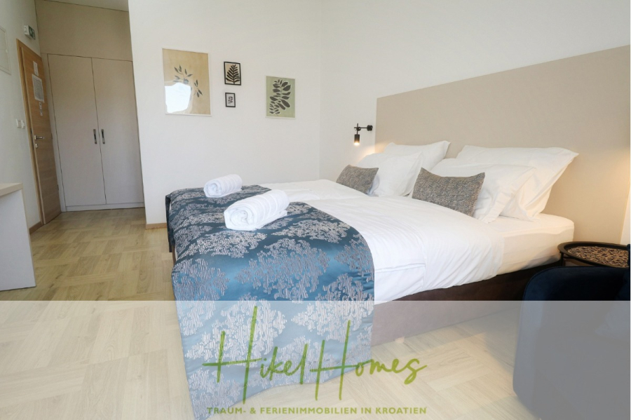 340m² Villa mit Pool auf der Insel Ciovo – vollständig möbiliert – auch Boutiquehotel möglich - Ein modernes, helles Schlafzimmer mit zwei nebeneinander stehenden Betten, die mit weißer Bettwäsche, gemusterten blauen Überwürfen und gerollten Handtüchern bezogen sind. Das Zimmer verfügt über minimalistische Wandkunst, Holzfußboden und einen Kleiderschrank. (45537)