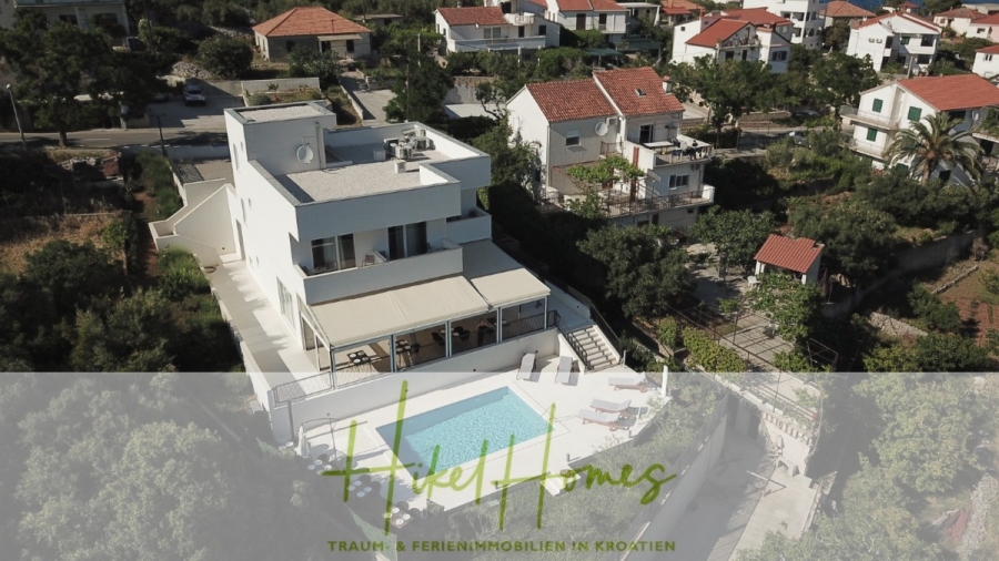 340m² Villa mit Pool auf der Insel Ciovo – vollständig möbiliert – auch Boutiquehotel möglich - Luftaufnahme einer modernen weißen Villa mit Swimmingpool, umgeben von Grünflächen und Nachbarhäusern, unter einem klaren Himmel. Textüberlagerung: "Hele Homes: Traum + Ferienimmobilien in Kroatien.". (45541)