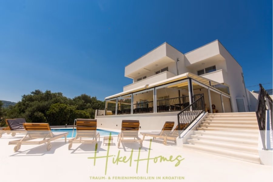 340m² Villa mit Pool auf der Insel Ciovo – vollständig möbiliert – auch Boutiquehotel möglich - Moderne weiße Villa mit großem Balkon und Glasgeländer, mehreren Sonnenliegen rund um den Pool unter strahlend blauem Himmel. Im Hintergrund sind grüne Hügel zu sehen. Das Bild enthält einen Textüberzug mit dem Hinweis „Hikel Homes“. (41622)