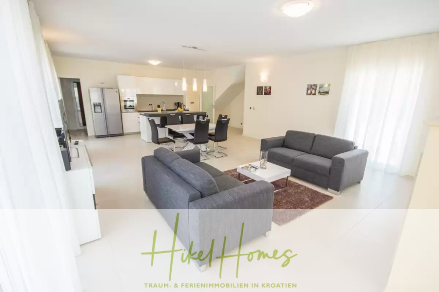 Villa im Mittelmeerstil mit 3 SZ, Pool, Dachterrasse mit Meerblick (1) - Moderner offener Wohn- und Küchenbereich mit zwei grauen Sofas, einem Esstisch mit schwarzen Stühlen, einer Kücheninsel und einem Kühlschrank. Heller Raum mit weißen Wänden, großen Fenstern und minimalistischem Dekor. (45824)