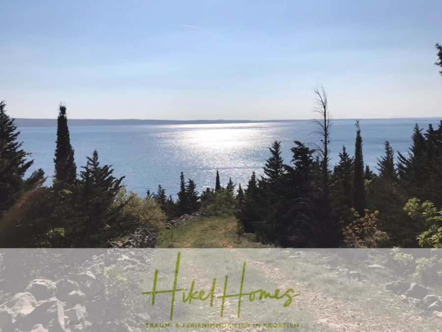 1437m² in erste Reihe zum Meer / Bauland zur Bebauung mit 2 Villen – Planung ist vorhanden - Blick auf ein schimmerndes Gewässer unter klarem Himmel, eingerahmt von Bäumen auf beiden Seiten eines Graspfades. Im Vordergrund zeigt eine transparente Überlagerung die Worte „HikeHomes“ und zusätzlichen Text. (42384)