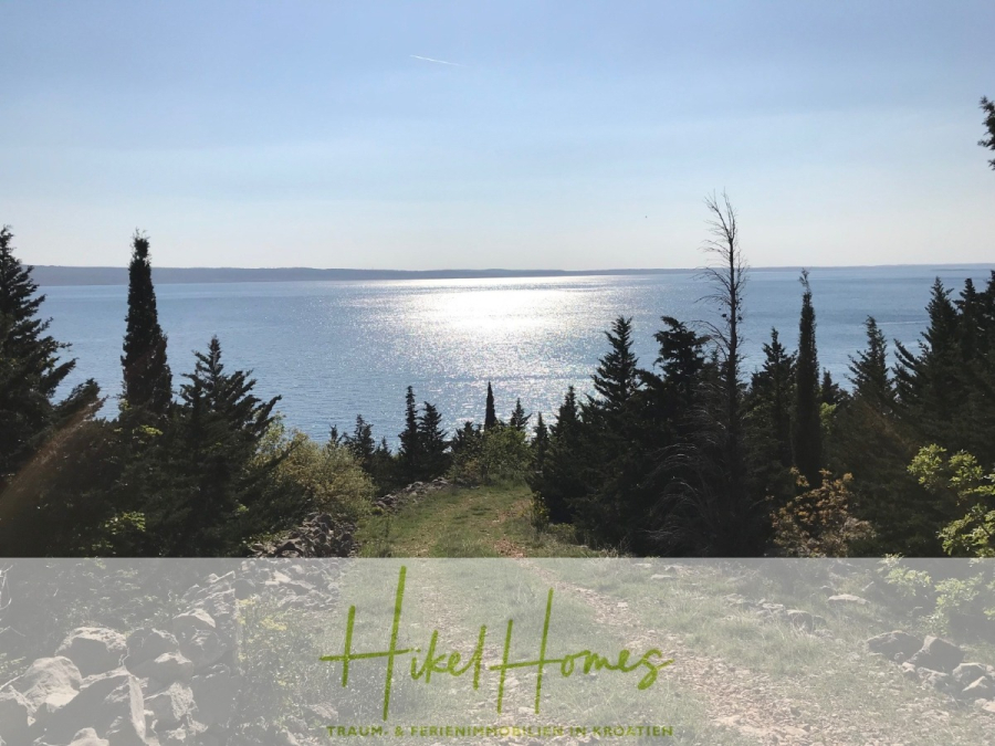 1437m² in erste Reihe zum Meer / Bauland zur Bebauung mit 2 Villen – Planung ist vorhanden - Ein malerischer Blick auf einen glitzernden blauen See oder ein Meer mit Sonnenlicht, das sich im Wasser spiegelt, eingerahmt von hohen, dunkelgrünen Bäumen und felsigem Gelände im Vordergrund. Die Worte "HikeHomes" und "Traum-Ferienimmobilien am Kroatien" stehen am unteren Rand. (45988)