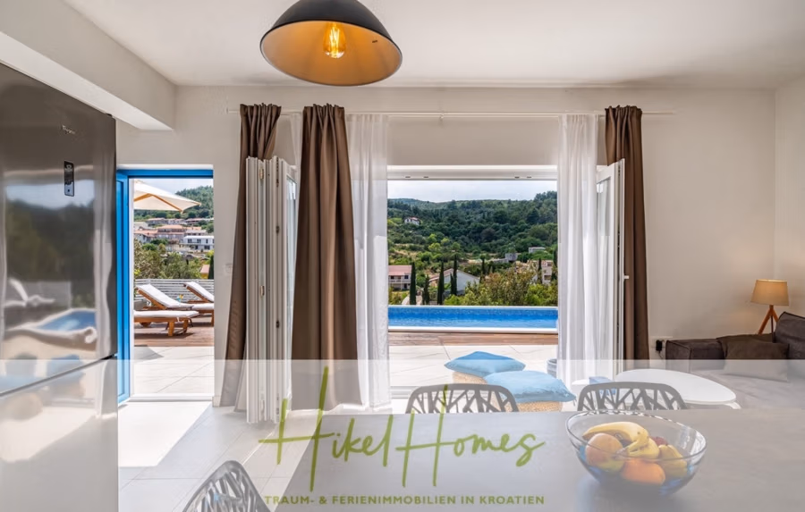 2 Meerblick Villen + freies Grundstück ideal zur Vermietungauf der Insel Dugi Otok jeweils mit Pool - Offener Wohnraum mit Blick auf die Poolterrasse durch große Doppeltüren. Der Innenraum ist modern eingerichtet und verfügt über einen Esstisch mit Obstschale und eine warme Lampe. Die Textüberlagerung lautet „Hikel Homes – Traum- & Ferienimmobilien in Kroatien“. (42898)