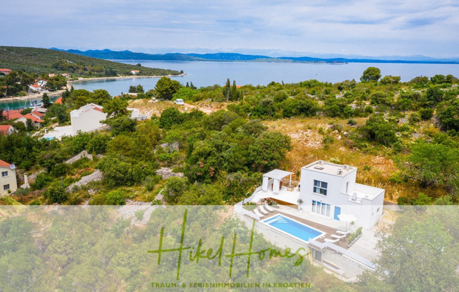 2 Meerblick Villen + freies Grundstück ideal zur Vermietungauf der Insel Dugi Otok jeweils mit Pool - Moderne weiße Villa mit Pool, umgeben von Grünflächen und Bäumen, mit Blick auf die Küste und das blaue Meer unter einem teilweise bewölkten Himmel. Das Logo "Hikel Homes" mit deutschem Text überlagert den Vordergrund. (44732)