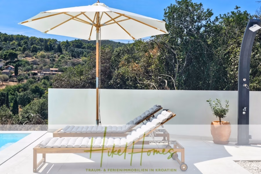 2 Meerblick Villen + freies Grundstück ideal zur Vermietungauf der Insel Dugi Otok jeweils mit Pool - Zwei gepolsterte Holzliegestühle mit Sonnenschirm neben einem Pool bieten Blick auf einen üppigen, baumbestandenen Hügel. In der Nähe befindet sich eine moderne Außendusche, und eine kleine Pflanze sorgt für Grün am Poolrand. Die Szenerie ist ruhig und einladend. (42908)