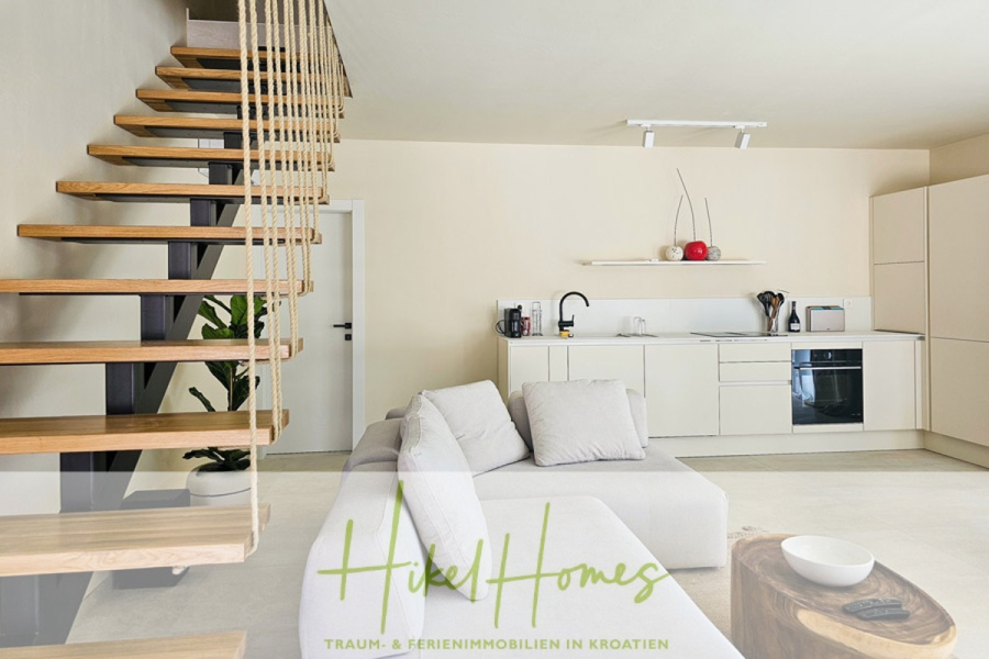 2 Meerblick Villen + freies Grundstück ideal zur Vermietungauf der Insel Dugi Otok jeweils mit Pool - Moderner Wohnraum mit minimalistischer Küche, hellen Schränken, schwarzem Ofen und einem L-förmigen Sofa. Eine offene Holztreppe mit Seilgeländer führt nach oben. Grüne Pflanzen und Dekoartikel setzen Akzente. Logo: "Hikel Homes" am unteren Rand. (44751)