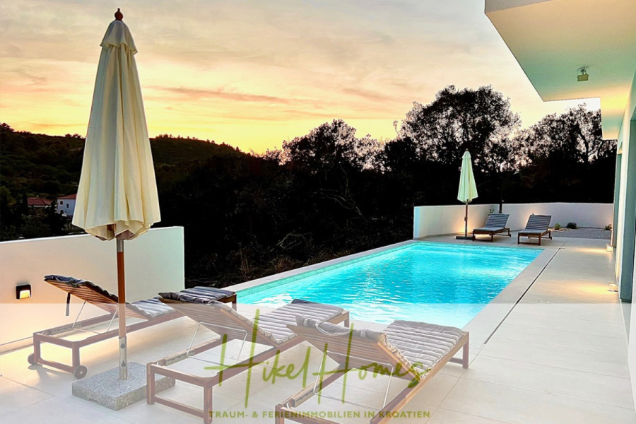 2 Meerblick Villen + freies Grundstück ideal zur Vermietungauf der Insel Dugi Otok jeweils mit Pool - Ein moderner Außenpool mit Liegestühlen und Sonnenschirmen ist bei Sonnenuntergang von Bäumen und weißen Wänden umgeben. Der Pool erstrahlt in sanftem Blau und schafft eine entspannte Urlaubsatmosphäre. (44755)