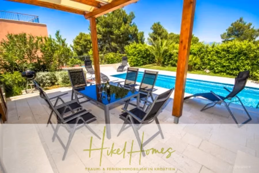 Villa im Mittelmeerstil mit 3 SZ, Pool, Dachterrasse mit Meerblick (7) - Außenterrasse mit einem Glasesstisch und acht schwarzen Stühlen unter einer Pergola, neben einem türkisfarbenen Swimmingpool. Der Bereich ist von üppigem Grün und einem strahlend blauen Himmel umgeben. Unten ist der Schriftzug „Hikel Homes“ eingelegt. (41655)