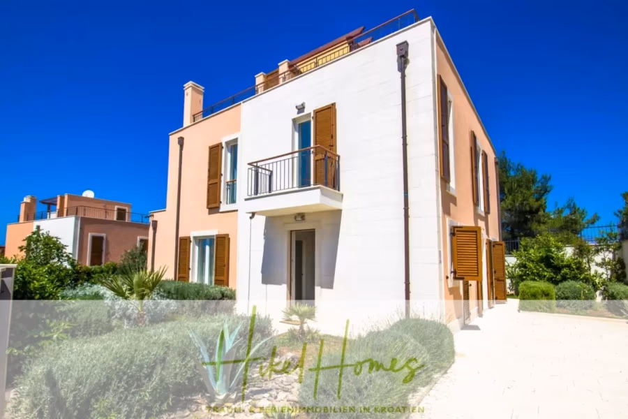 Villa im Mittelmeerstil mit 3 SZ, Pool, Dachterrasse mit Meerblick (7) - Modernes zweistöckiges Haus mit pfirsich-weißer Fassade, Holzläden und kleinem Balkon. Umgeben von üppigem Grün und strahlend blauem Himmel. Das Logo „Tilia Homes“ überlagert das Bild unten. (41654)