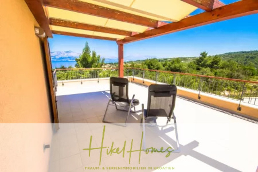 Villa im Mittelmeerstil mit 3 SZ, Pool, Dachterrasse mit Meerblick (7) - Eine geräumige Terrasse mit zwei schwarzen Stühlen unter einer hölzernen Pergola überblickt eine malerische Landschaft mit Bäumen, Hügeln und entferntem Wasser unter einem klaren blauen Himmel. (44829)