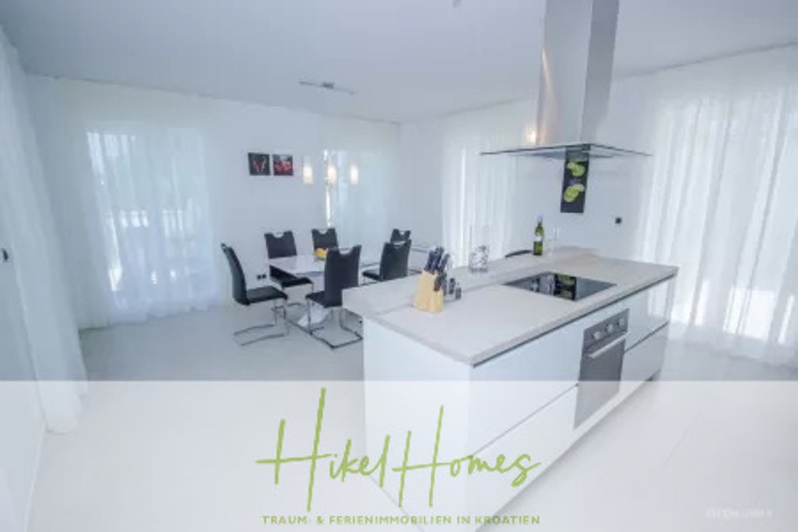 Villa im Mittelmeerstil mit 3 SZ, Pool, Dachterrasse mit Meerblick (7) - Moderne weiße Küche mit Insel, Herd und Dunstabzugshaube. Essecke mit sechs schwarzen Stühlen und einem rechteckigen Tisch im Hintergrund. Große Fenster mit durchsichtigen weißen Vorhängen lassen natürliches Licht herein. (44835)